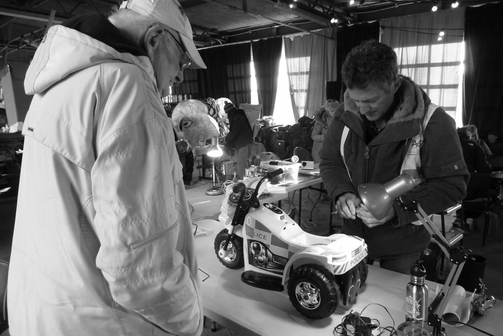 Two men standing at a table looking at a child's police bike