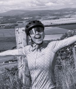 A woman wearing a cycling helmet and glasses smiles.